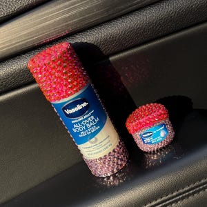 May include: Two pink and white jeweled containers of Vaseline Healing Jelly All-Over Body Balm Jelly Stick. The larger container is a tube and the smaller container is a jar.