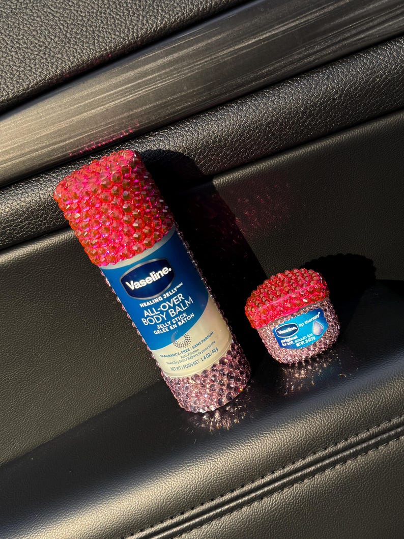 May include: Two pink and white jeweled containers of Vaseline Healing Jelly All-Over Body Balm Jelly Stick. The larger container is a tube and the smaller container is a jar.