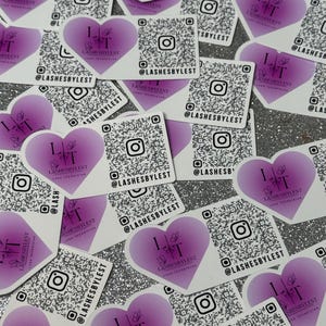 May include: A collection of heart-shaped stickers with a purple gradient. Each sticker features a stylized 'I <3 T' design with the text 'LASHESBYLEST LASH TECHNICIAN' and a QR code. The stickers are scattered on a sparkly surface.