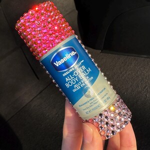 May include: A pink and silver embellished bottle of Vaseline Healing Jelly All-Over Body Balm Jelly Stick. The bottle is labelled "Vaseline. Healing Jellyte All-Over Body Balm Jelly Stick Gel&eacute;e en Baton Fragrance-Free/Sans Parfum Anti-Fricti Heals Dry Skin/R&eacute;pare peau s&egrave;che Net Wt/Poids Net 1.4 oz/40g"