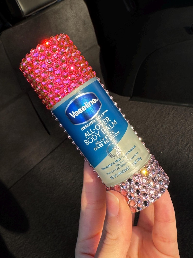May include: A pink and silver embellished bottle of Vaseline Healing Jelly All-Over Body Balm Jelly Stick. The bottle is labelled "Vaseline. Healing Jellyte All-Over Body Balm Jelly Stick Gel&eacute;e en Baton Fragrance-Free/Sans Parfum Anti-Fricti Heals Dry Skin/R&eacute;pare peau s&egrave;che Net Wt/Poids Net 1.4 oz/40g"