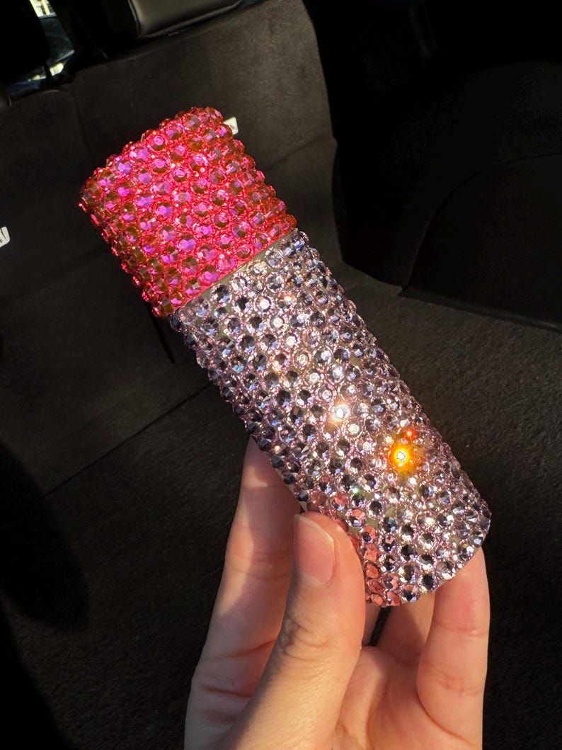 May include: A pink and clear bottle covered in rhinestones. The bottle is decorated with small, iridescent rhinestones.