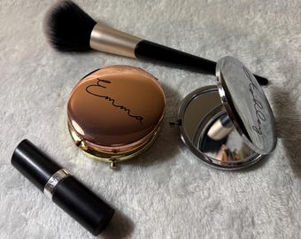 May include: Two compact mirrors with personalized engravings. One mirror is rose gold with the name "Emma" engraved on it. The other mirror is silver with the name "Holly" engraved on it.