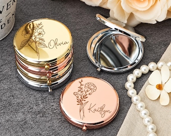 May include: A stack of round metal compact mirrors in gold, rose gold, and silver finishes. The top gold mirror is engraved with a floral design and the name Olivia. A rose gold mirror features a floral engraving and the name Kaitlyn.
