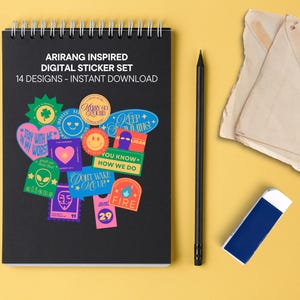 May include: A black spiral-bound notebook featuring the text ARIRANG INSPIRED DIGITAL STICKER SET 14 DESIGNS - INSTANT DOWNLOAD and a collection of colorful graphic stickers with various shapes, symbols, and phrases, alongside a black pencil.