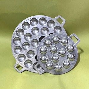 May include: Two silver aluminum baking pans with round depressions for making small cakes or pastries. The larger pan has 24 depressions and the smaller pan has 16 depressions.