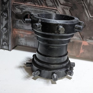 May include: A black metal pipe fitting with multiple bolts and a textured surface.