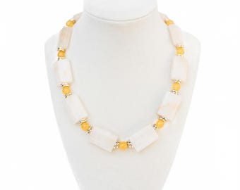 May include: A necklace displayed on a white mannequin. The necklace features rectangular, off-white beads interspersed with smaller, round, yellow beads. Silver-colored metal accents connect the beads. The necklace is a jewelry item.