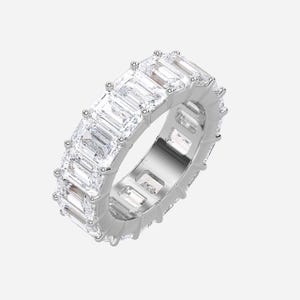 May include: A silver eternity ring featuring a continuous row of emerald-cut, clear gemstones. The ring's band is also silver, with a polished finish. The gemstones are set closely together, creating a sparkling, elegant look.