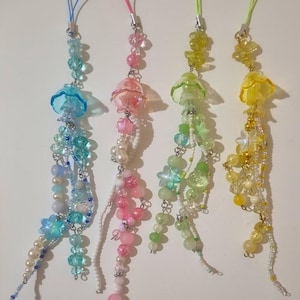 Op de afbeelding: Vier kralenhangers in blauw, roze, groen en geel. Elke hanger heeft een doorschijnende bloem of kwalachtige top, met bungelende kralen en parels. De hangers hebben gekleurde koorden om op te hangen.