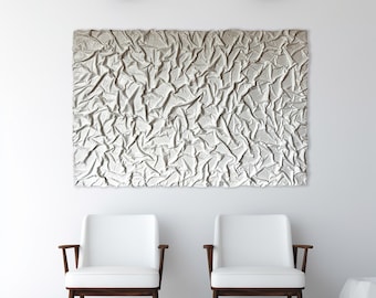 Könnte beinhalten: Zwei weiße Stühle mit Holzbeinen und Armlehnen, die sich gegenüber vor einer weißen Wand mit zwei schwarzen Pendelleuchten darüber befinden. Ein großes abstraktes silbernes Kunstwerk hängt an der Wand hinter den Stühlen.