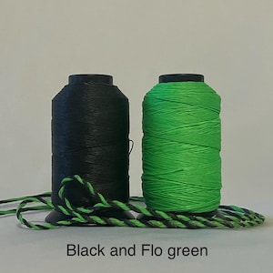 May include: Two spools of thread, one black and one bright green, with a length of black and green twisted cord in the foreground.