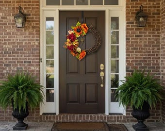 May include: A dark brown front door with a decorative wreath featuring sunflowers and other colorful flowers. The door is flanked by two ferns in black urn planters. The house has a brick exterior and a welcome mat.