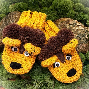 May include: A pair of yellow and brown crocheted mittens with fuzzy brown ears and googly eyes. The mittens have black noses and are perfect for keeping your hands warm in the winter.