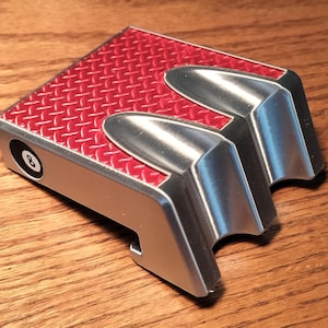 May include: A rectangular, silver metal object with a red diamond-plate textured top. The object has two curved, silver protrusions and the number 8 printed on the side. Likely a novelty item.