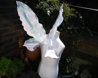May include: White fairy wings with iridescent green accents are displayed on a white dress form. The wings have a delicate, flowing design, perfect for costume or cosplay. The wings are made of a sheer, lightweight material.