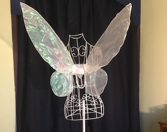 May include: A white and iridescent butterfly costume wing set on a wire stand. The wings are made of sheer fabric and have a delicate, ethereal look.