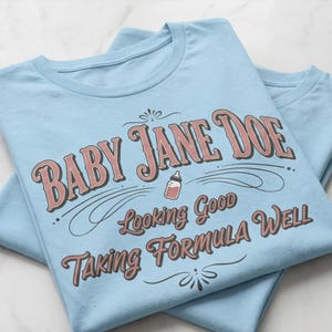 The pitt Baby Jane Doe funny slogan t shirt with baby bottle graphic, folded blue graphic tees stacked on marble background, clean product mockup image highlighting vintage typography humor design inspired by the pitt aesthetic and modern casual fashion trend