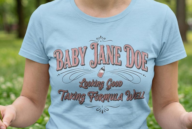 The Pitt Baby Jane Doe funny slogan t shirt with baby bottle graphic, woman wearing blue graphic tee outdoors in park setting, casual lifestyle image with soft natural greenery background, vintage typography humor design inspired by the pitt aesthetic and modern everyday fashion trend