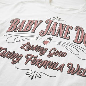 Baby Jane Doe funny slogan t shirt with baby bottle graphic, angled close up of blue graphic tee showing vintage typography design and soft fabric texture, detailed product image highlighting print quality inspired by the pitt aesthetic and casual fashion trend