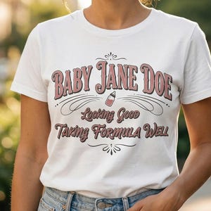 The Pitt Baby Jane Doe funny slogan t shirt with baby bottle graphic, woman wearing classic white graphic tee outdoors in soft sunlight, casual lifestyle image with vintage typography humor design inspired by the pitt aesthetic and modern everyday fashion trend