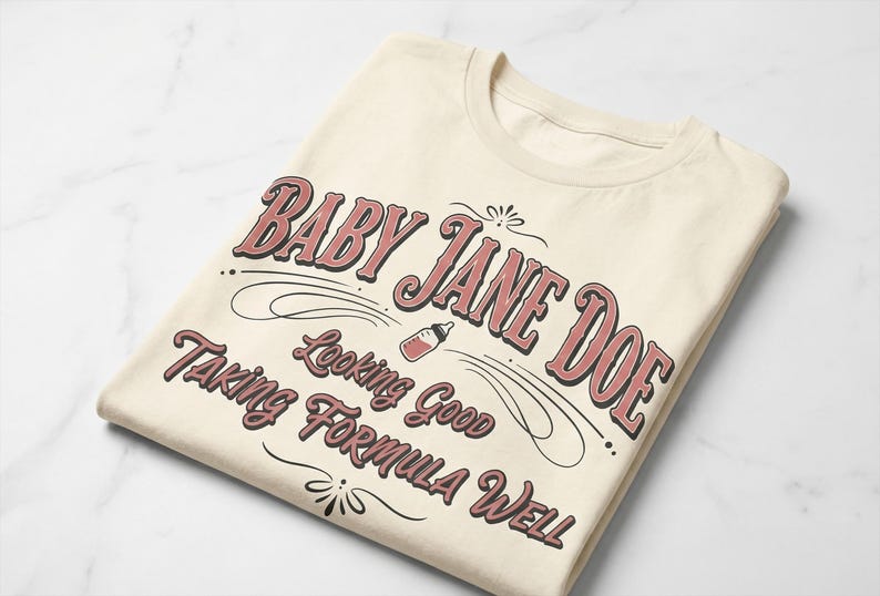 The Pitt Baby Jane Doe funny slogan t shirt with baby bottle graphic, folded cream graphic tee flat lay on clean background, product display image highlighting vintage typography humor design inspired by the pitt aesthetic and trendy casual fashion style