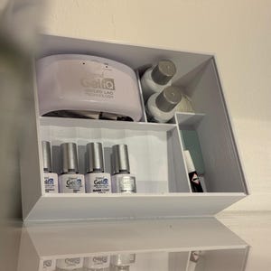 May include: A white storage box filled with nail care items. It includes a UV LED lamp, nail polish bottles, and other manicure essentials. The lamp has the text "Depend Gelia UV LED LAC TECHNOLOGY" printed on it.