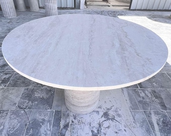 May include: A large, round, white marble table top with a light gray veining pattern. The table top is supported by a thick, white marble pedestal.
