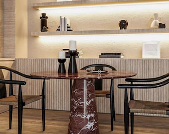 May include: A modern dining room set featuring a round marble table with a red and white pattern, supported by a conical base. The table is surrounded by black chairs with woven seats. Shelves with decorative items are in the background.