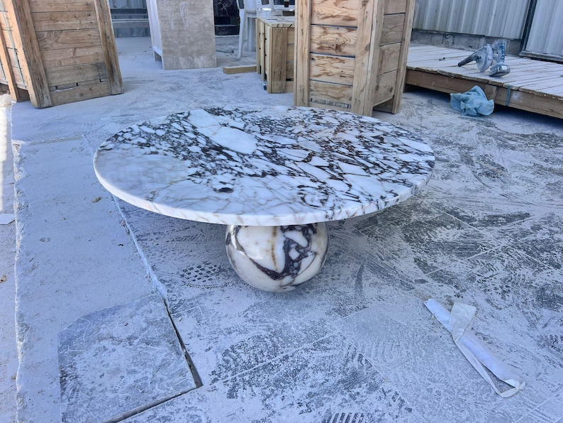 May include: A round marble table with a white and black patterned top. The table is supported by a spherical base with similar veining. The table is a statement piece for any living space.