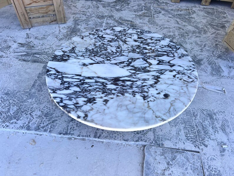 May include: A round marble table with a white and black patterned surface. The table has a polished finish and is set against a gray background. The table's design is a striking contrast of light and dark tones.