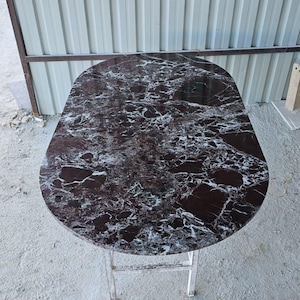 Pode incluir: Mesa pequena, oval, com tampo em mármore castanho escuro e veios brancos. Possui uma estrutura metálica dobrável. A mesa mede aproximadamente 76 cm de comprimento e 51 cm de largura. Ideal para espaços pequenos.