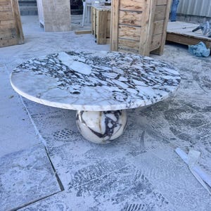 May include: A round marble table with a white and black patterned top. The table is supported by a spherical base with a similar marble design. The table's diameter is approximately 48 inches.