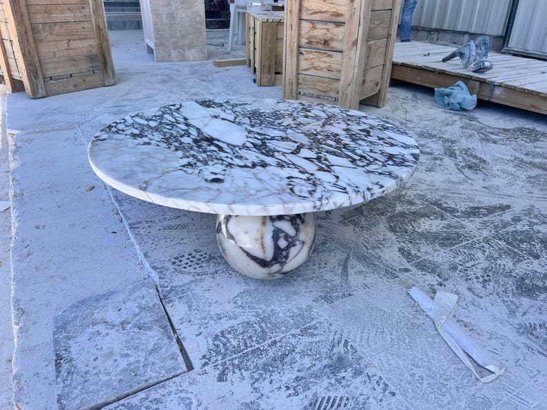 May include: A round marble table with a white and black patterned top. The table is supported by a spherical base with a similar marble design. The table's diameter is approximately 48 inches.