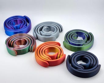 May include: Six spiral-shaped objects in various colors, including blue, green, orange, and gray. Each object has a unique color gradient. The objects are arranged on a white surface.