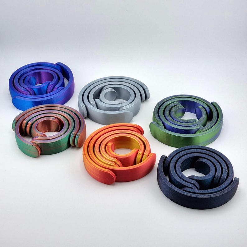 May include: Six spiral-shaped objects in various colors, including blue, green, orange, and gray. Each object has a unique color gradient. The objects are arranged on a white surface.