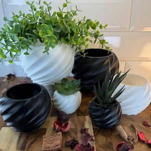 May include: Five white and black swirl planter pots in different sizes with various plants. The pots are made from a textured material and feature a unique swirl design. The plants include a variety of succulents and greenery.