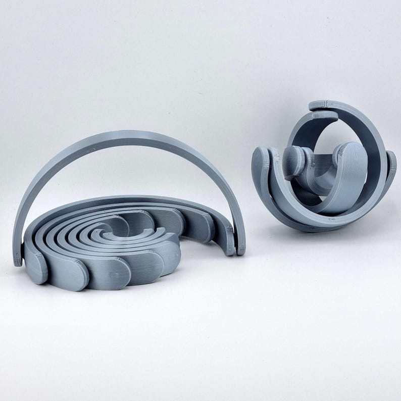 May include: Two gray, abstract, 3D-printed sculptures. One is a spiral with a handle, the other is a spherical shape with curved elements. The objects are on a white background.