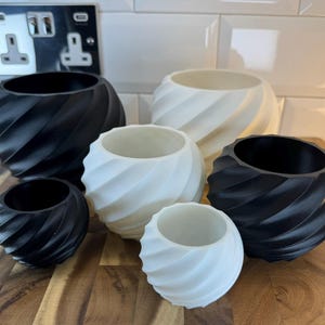 Peut inclure: Ensemble de six pots de fleurs décoratifs de différentes tailles et couleurs. Les pots présentent un design en spirale et sont en noir et blanc. Ils sont fabriqués dans un matériau lisse et sont disposés sur une surface en bois.