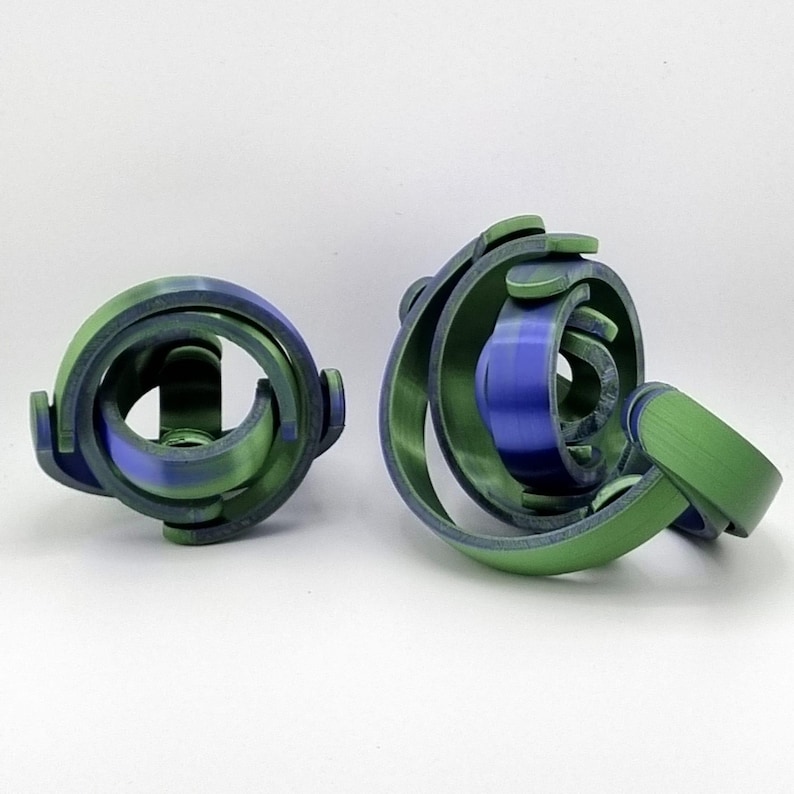 May include: Two abstract, 3D-printed sculptures. One is a sphere-like shape with green and blue swirls. The other is a similar design, with a blue center and green outer rings. The objects are on a white background.