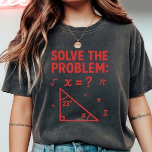 May include: Dark gray t-shirt with the text "SOLVE THE PROBLEM:" in red, along with mathematical symbols and a triangle diagram. The shirt has a crew neck and short sleeves.