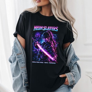 Puede incluir: Camiseta negra con un gráfico de un personaje femenino de anime empuñando una espada rosa brillante. El texto "NEON SLAYERS" está encima de la imagen, con "WORLD TOUR: SEOUL - TOKYO - CYBERSPACE" debajo.