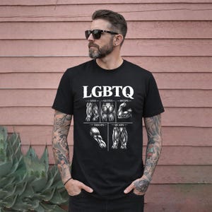 May include: Black t-shirt featuring the word "LGBTQ" in white, with illustrations of muscle groups beneath. The illustrations include legs, glutes, biceps, triceps, and quads. The shirt is worn by a person wearing sunglasses.