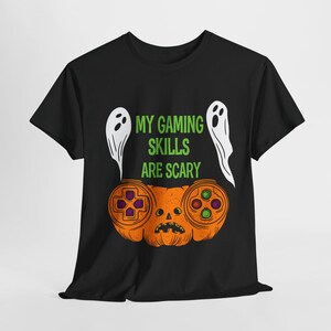 Op de afbeelding: Zwart T-shirt met een Halloween-ontwerp. De afbeelding toont een pompoen in de vorm van een gamecontroller, twee witte spookfiguren en de groene tekst "MY GAMING SKILLS ARE SCARY".