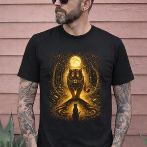 May include: Black t-shirt featuring a golden tiger design under a full moon. The artwork includes a silhouette of a cat at the bottom. The design is set against a backdrop of a forest, creating a mystical and artistic aesthetic.
