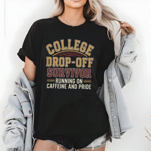 Op de afbeelding: Zwart t-shirt met de tekst "COLLEGE DROP-OFF SURVIVOR RUNNING ON CAFFEINE AND PRIDE" in goud, bordeauxrood en wit. Een casual t-shirt, geschikt voor dagelijks gebruik.