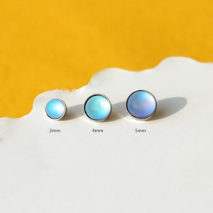 May include: Three iridescent blue body jewelry beads in different sizes: 3mm, 4mm, and 5mm. The beads are round and have a smooth, shiny finish.