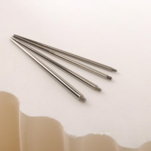 May include: Four silver metal piercing bars of different lengths. The bars have a threaded end.