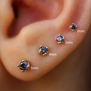 May include: Close-up of an ear with four gold stud earrings. Each earring features a round, iridescent gemstone. The sizes are 2mm, 3mm, 4mm, and 5mm. The earrings are set in a simple, four-prong gold setting.