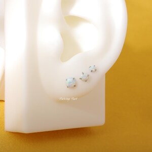 May include: Three white opal earrings with silver posts. The earrings are shown on a white ear model.